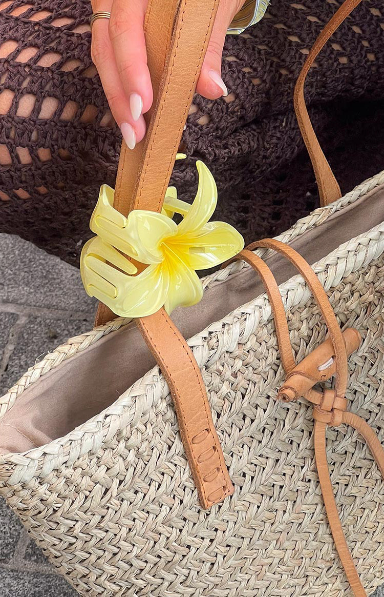 Yellow frangipani flower clip showing translucent petals, darker yellow center, and the claw mechanism attached to a strap
