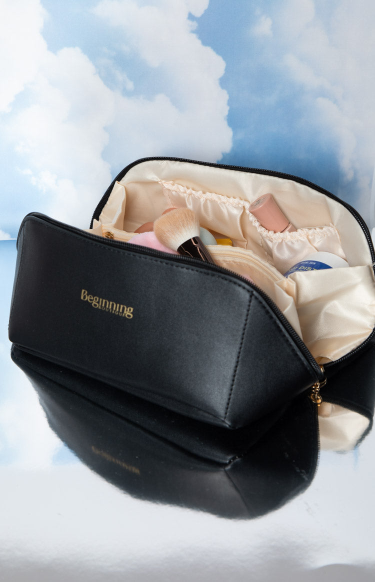 Close-up of the black cosmetic bag's gold zipper pull with a round charm and structured bottom corner