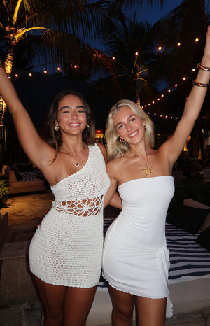 Front view of a cream crochet mini dress with an asymmetrical one-shoulder neckline and intricate floral cutout detail at the waist