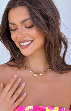 Close-up of a gold chain necklace with various shell charms and small white pearls