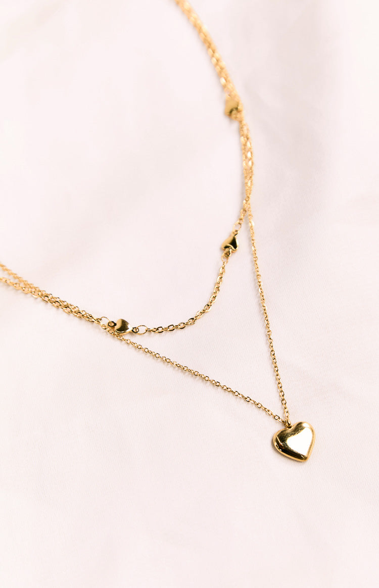 Close-up of the shiny gold heart pendant and the small heart details on the double chain necklace
