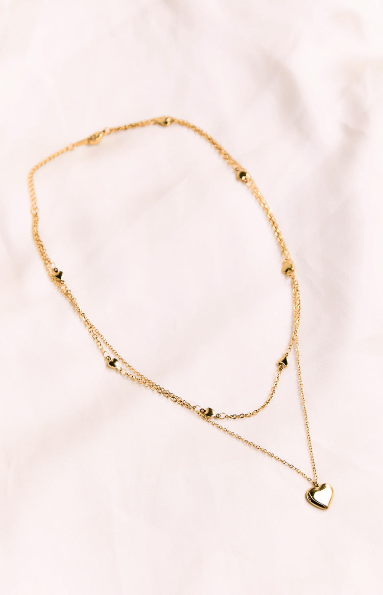 Gold double chain necklace with a heart pendant and small heart details along both chains, flat lay