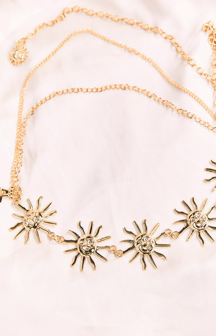 A gold-toned chain belt featuring multiple large sun charms with faces and a smaller sun charm near the closure. The chains are adjustable and styled to layer.