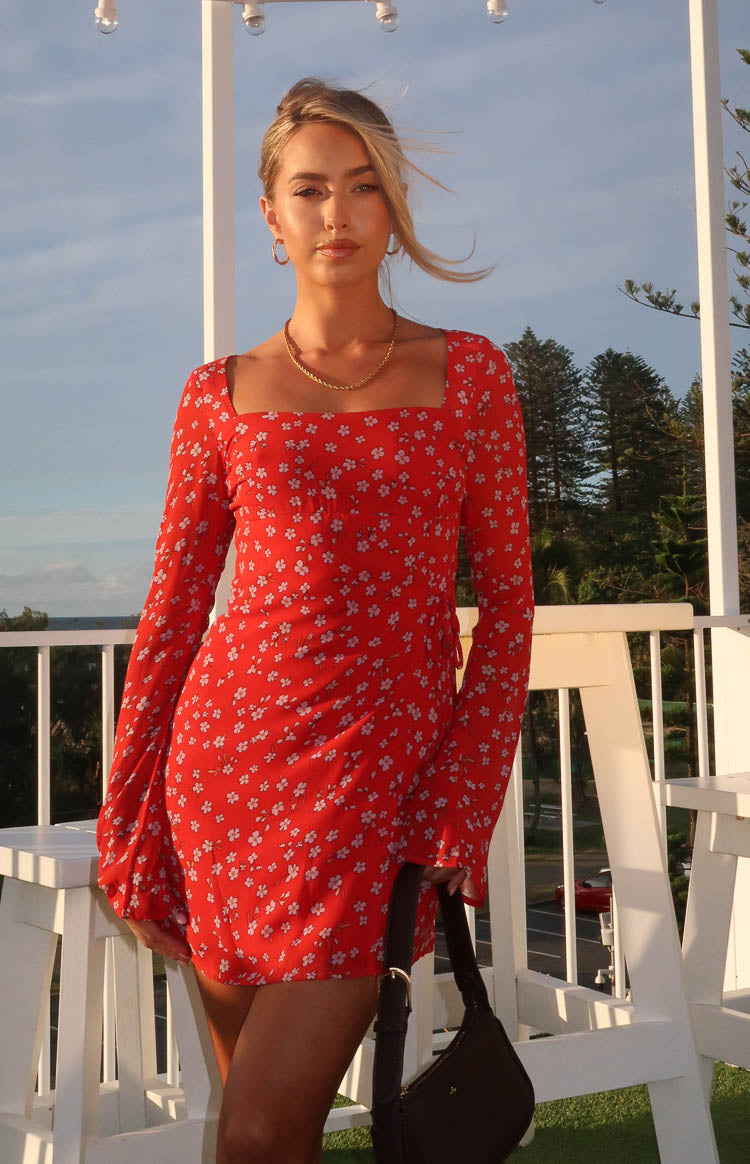 Red mini dress with a square neckline, long sleeves, white floral print, and a subtle side tie detail