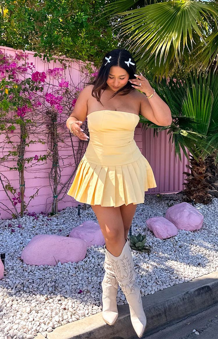 Front view of a yellow strapless mini dress featuring a fitted bodice and a wide pleated skirt