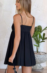 Side view of a black mini dress with thin adjustable spaghetti straps, a square back neckline, and a gathered A-line skirt