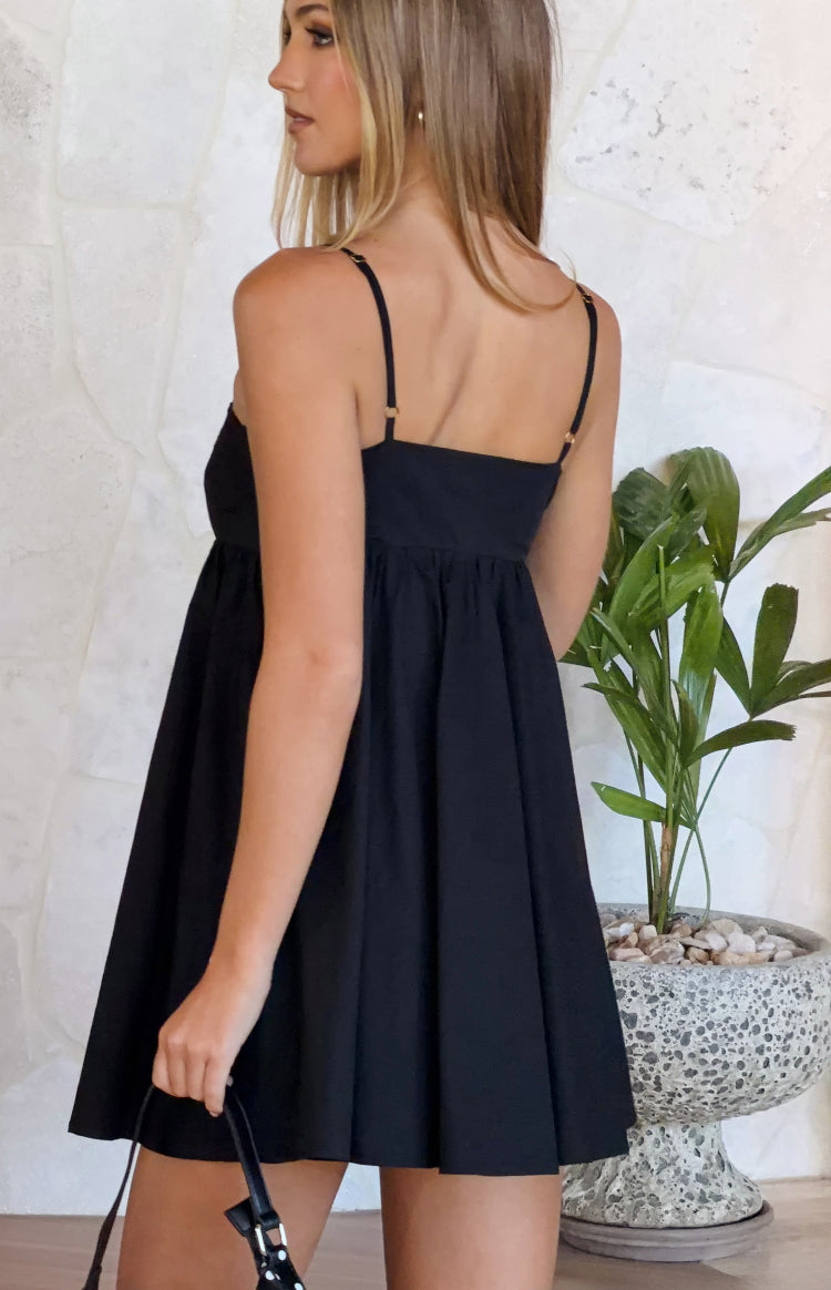 Side view of a black mini dress with thin adjustable spaghetti straps, a square back neckline, and a gathered A-line skirt