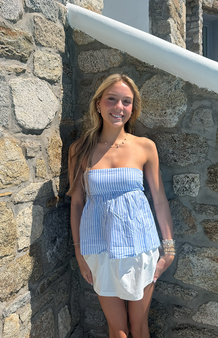 Front view of a light blue and white striped strapless top with a gathered waist and flowy peplum hem