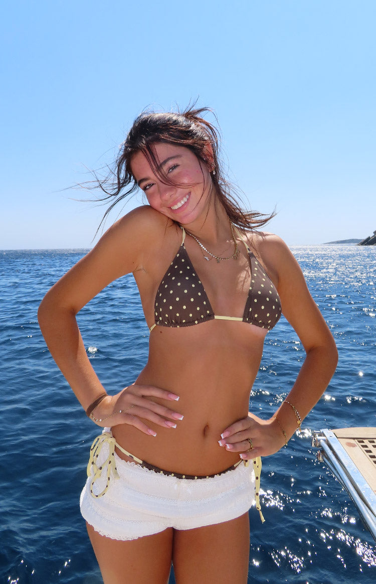 Front view of a brown polka dot triangle bikini top with thin yellow spaghetti straps and yellow trim