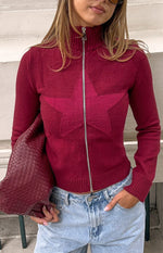 Close-up of a burgundy knit sweater with a large textured star pattern and a silver full zip front