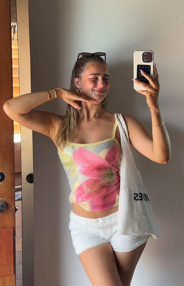Front view of a cropped yellow sequin tank top with a large pink floral design and thin yellow spaghetti straps