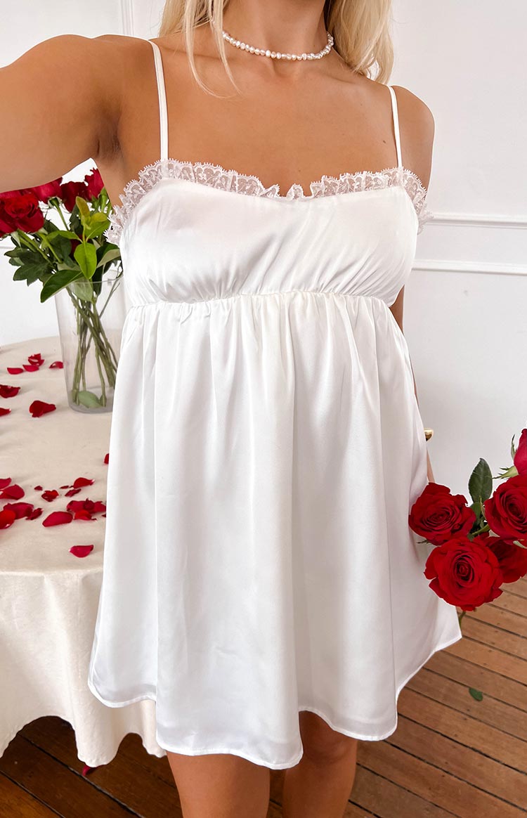 Front view of a white satin mini dress with delicate lace trim on the bust and a gathered empire waist