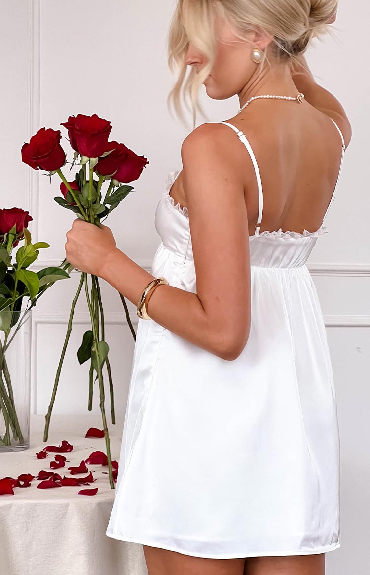 Rear view of a white satin mini dress with thin spaghetti straps, ruffled lace trim, and a gathered waist
