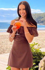 A brown off-the-shoulder mini-dress with a white polka dot pattern and ruffled detailing on the sleeves and neckline. This dress is suitable for a casual summer day or a vacation.