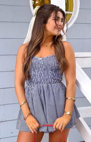 Model is wearing a navy and white gingham playsuit featuring a shirred bodice
