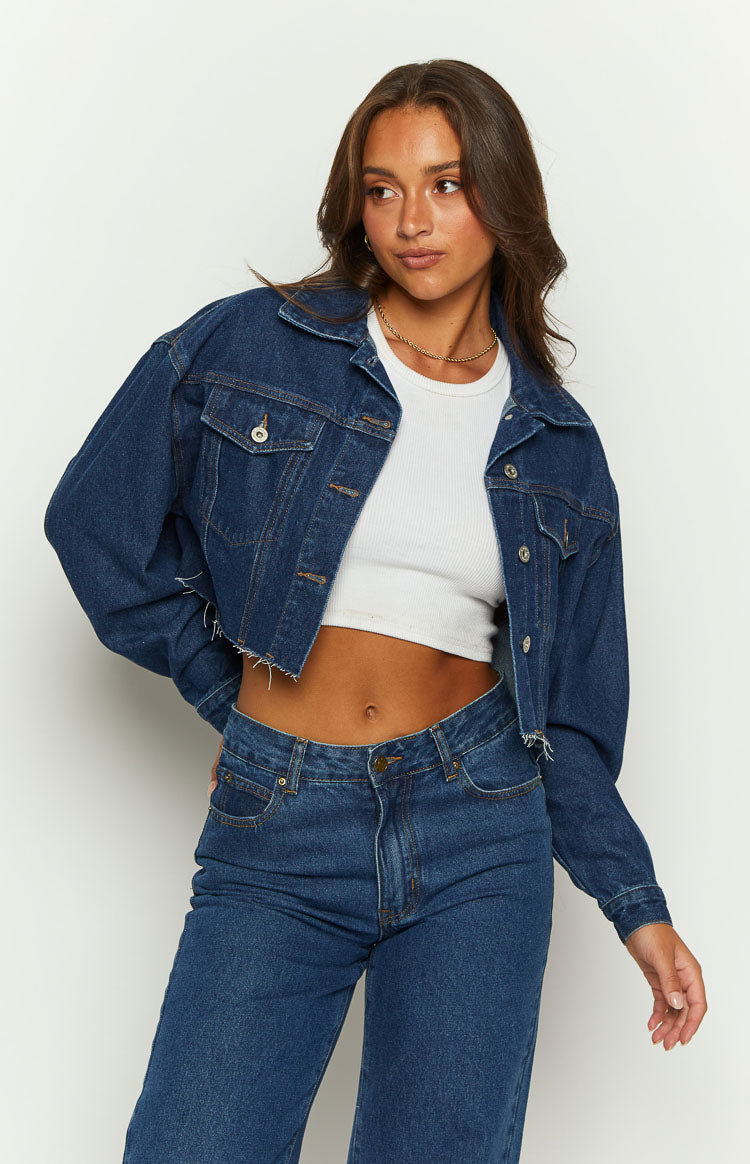Front view of a dark wash denim cropped jacket with a relaxed fit and frayed raw hem