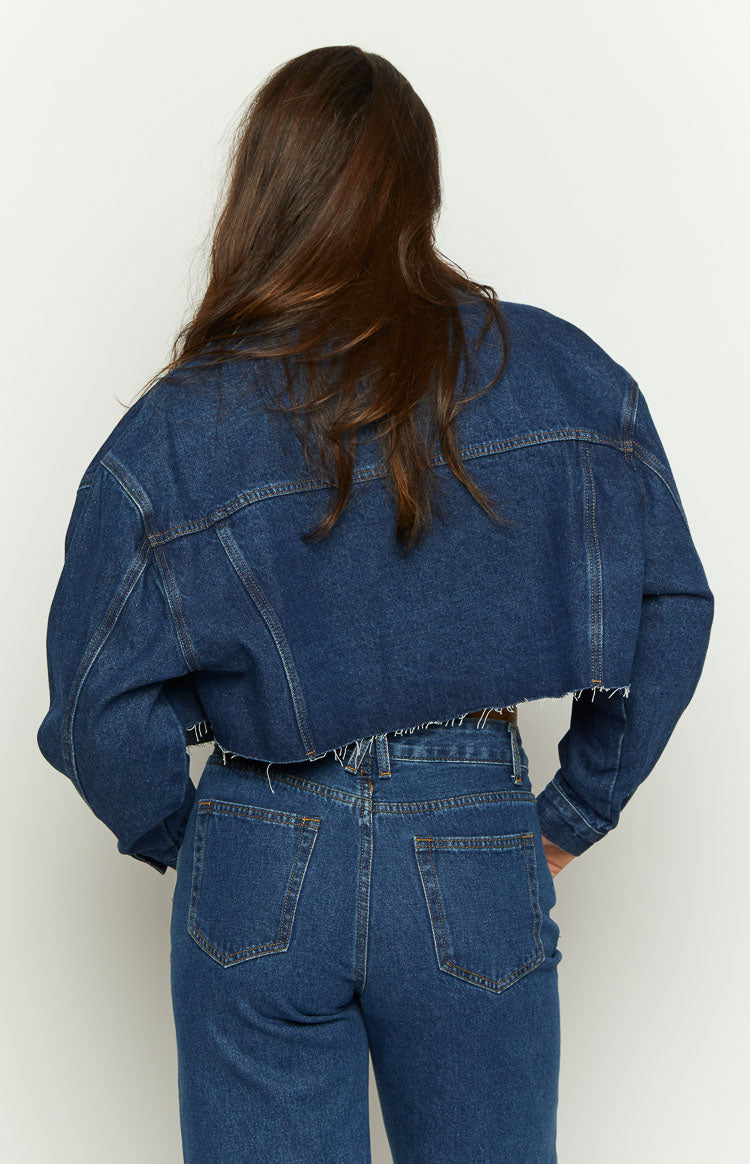 Dark wash denim cropped jacket with long sleeves and a raw, distressed hem
