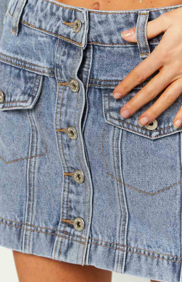 Front view of a mid-wash denim cargo mini skirt with a button-front closure and flap pockets