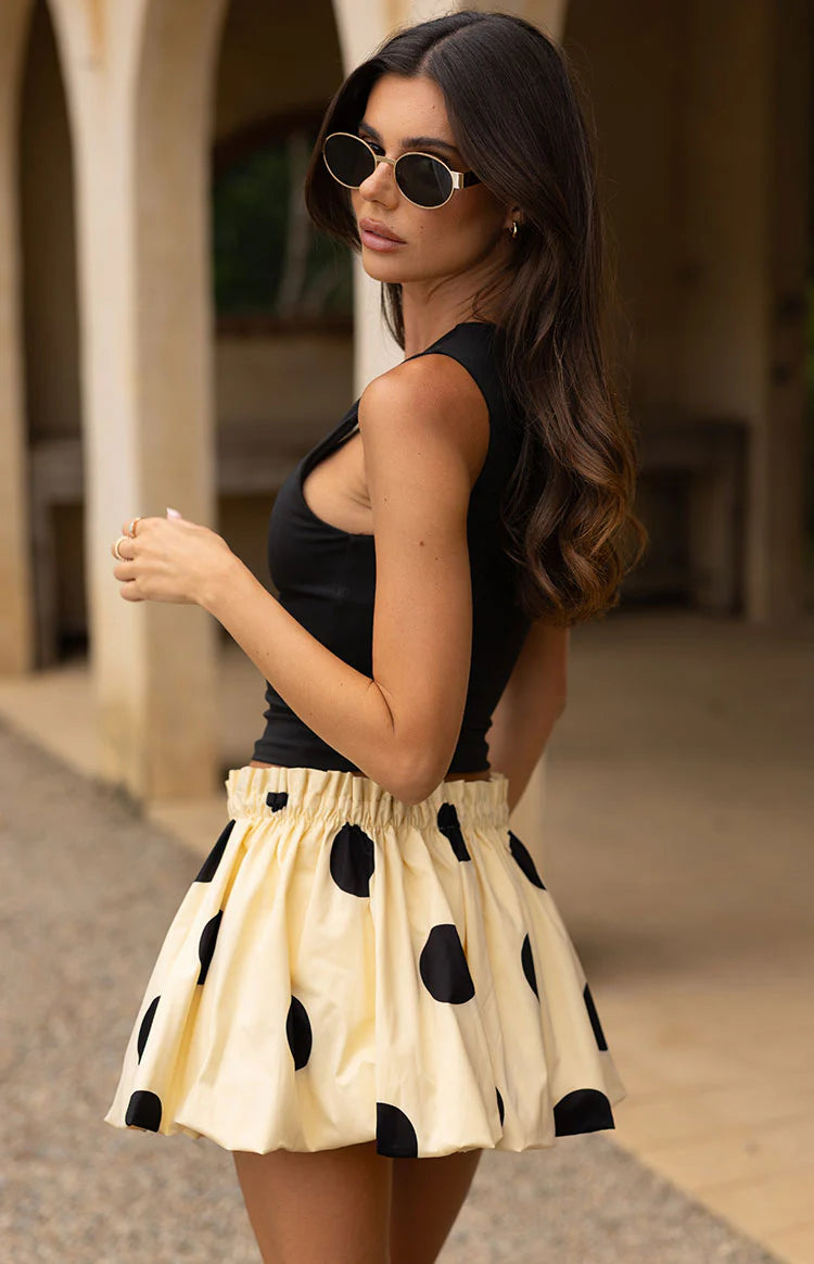 Side view of a yellow mini skirt with black polka dots, featuring an elasticated ruched waist and a voluminous bubble hem