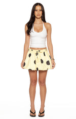 Front view of a yellow mini skirt with black polka dots, a ruched drawstring waist, and a bubble hem
