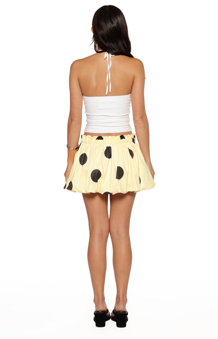 Back view of a yellow mini skirt with black polka dots, a shirred elastic waistband, and a bubble hem