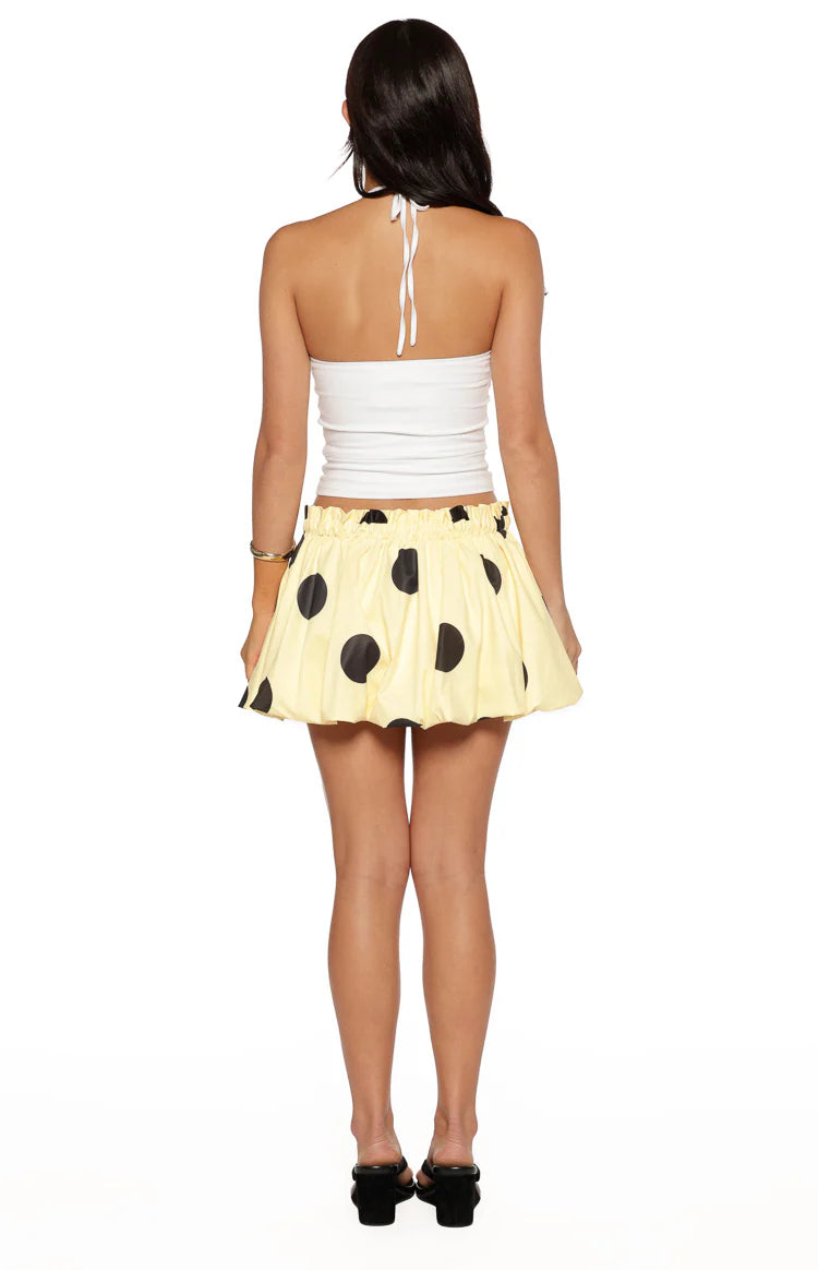 Back view of a yellow mini skirt with black polka dots, a shirred elastic waistband, and a bubble hem