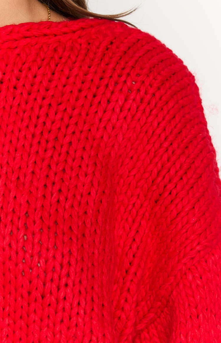 Close-up of the chunky red knit texture and visible stitches of the cardigan's shoulder