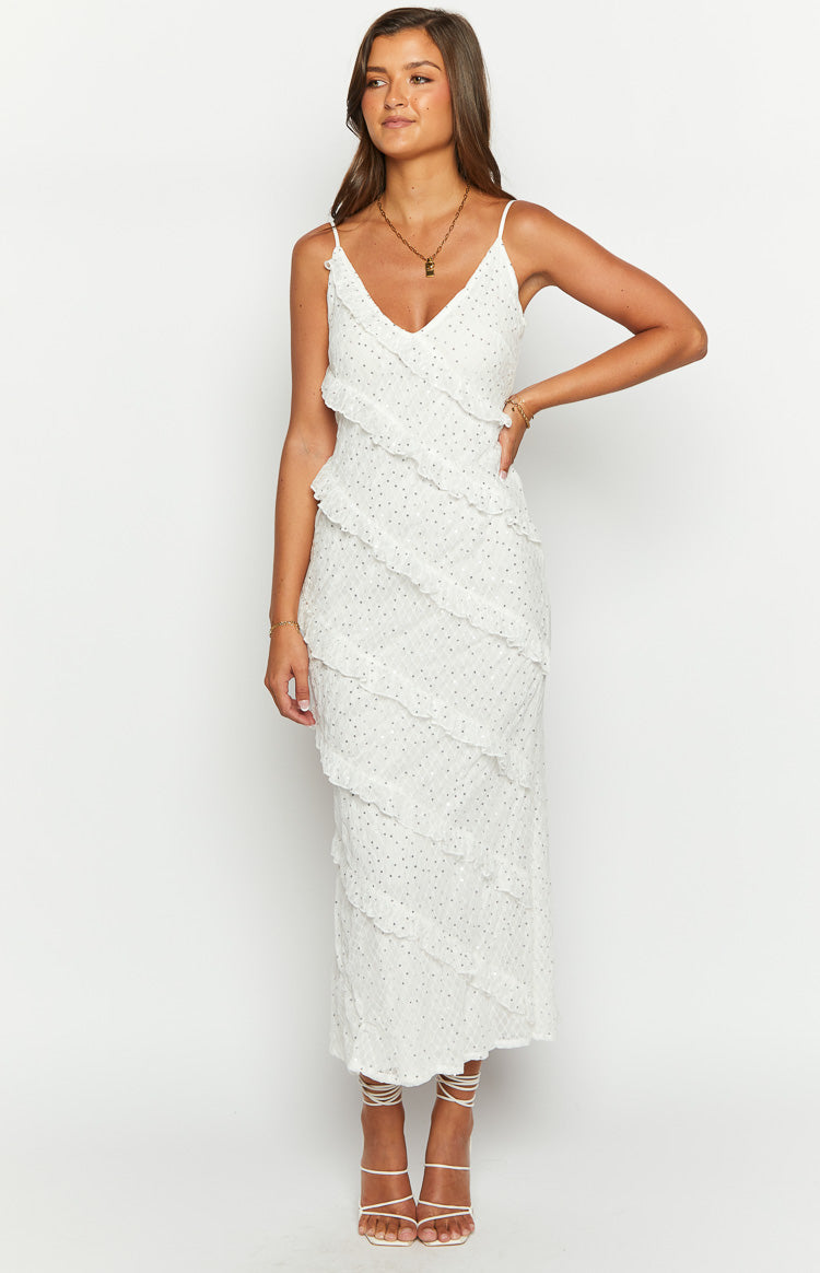 Cascading asymmetrical ruffles on a white V-neck maxi dress with thin spaghetti straps and subtle silver dots