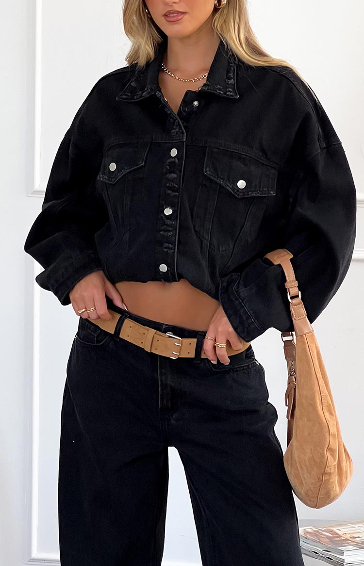 Close-up of the black denim jacket showing the cropped length, silver buttons, and distressed collar