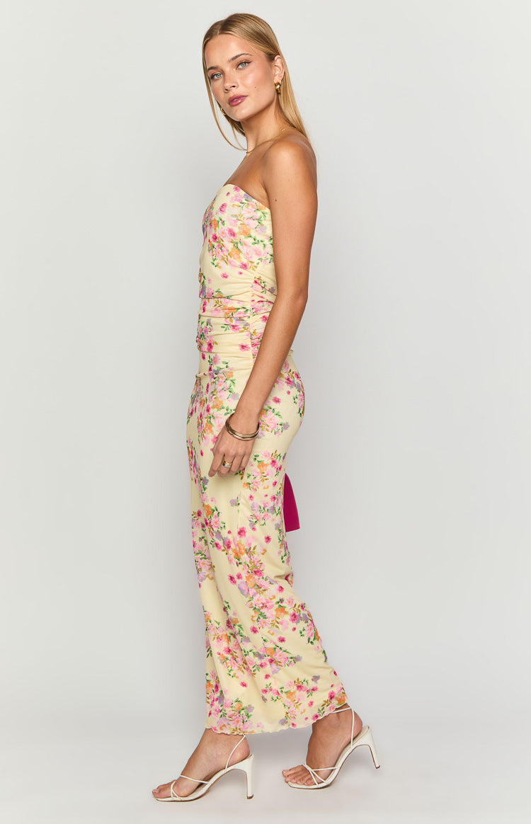 Side view of a yellow floral strapless maxi dress with ruched detailing and a fuchsia tie
