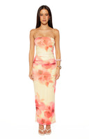 Our model wearing a strapless maxi-dress in a light yellow color featuring an abstract floral print in shades of pink and coral with a ruched fitted bodice and a bodycon silhouette.