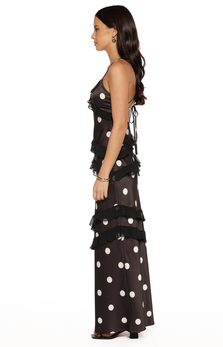 Side view of a black polka dot maxi dress with sheer black ruffle tiers and delicate tie-back spaghetti straps