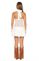 Rear view of a white mini dress with a halter neck tie, floral lace bodice, and gathered skirt