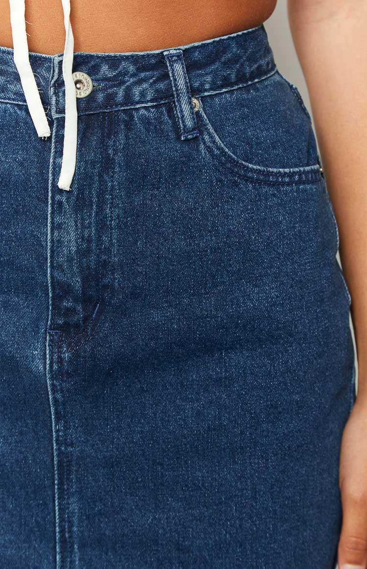 Close-up of the dark wash denim midi skirt's waistband, front button closure, and classic curved pocket