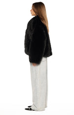 Side view of a black faux fur jacket showing its shaggy texture and cropped length