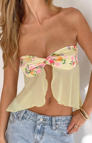 Close-up of the yellow floral strapless top with a twisted knot bust and sheer flowy fabric with a scalloped hem