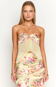 Close-up of the yellow floral strapless top with a twisted knot bust and sheer flowy fabric with a scalloped hem