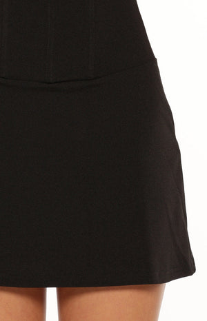 Close-up of the black crepe mini dress skirt, showing the textured fabric, structured waist seam, and subtle flare