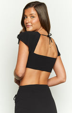Back view of a black crop top with a square back, short ruffled cap sleeves, and a tie closure with gold toggles