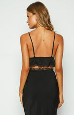 Rear view of a black crop top with thin adjustable spaghetti straps, a ruffled back, and two rows of delicate lace trim