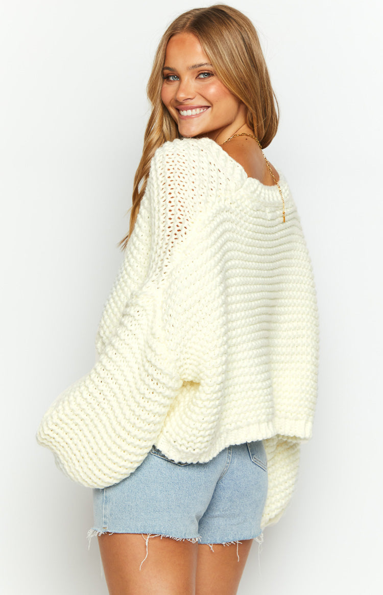 Side view of a white chunky knit cardigan with a wide neckline worn off one shoulder and voluminous sleeves