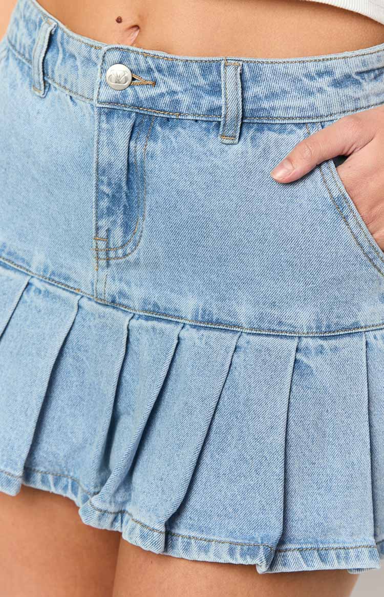 Close-up of the light wash denim mini skirt showing the button closure, front pockets, and pleated design