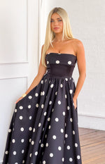 Angled front view of a black satin strapless maxi dress with white polka dots, fitted bodice, and full skirt with pockets