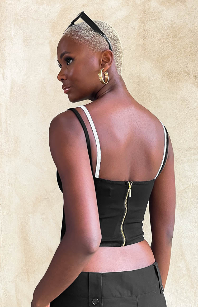 Back view of a black double layered crop top with a gold zipper closure and thin black and white spaghetti straps