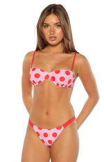 Front view of pink bikini bottoms with red polka dots, featuring thin red side straps and a low-rise cut