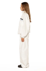 Side view of a cream funnel neck jacket with black and light blue chest stripes, showing oversized fit and wide sleeves