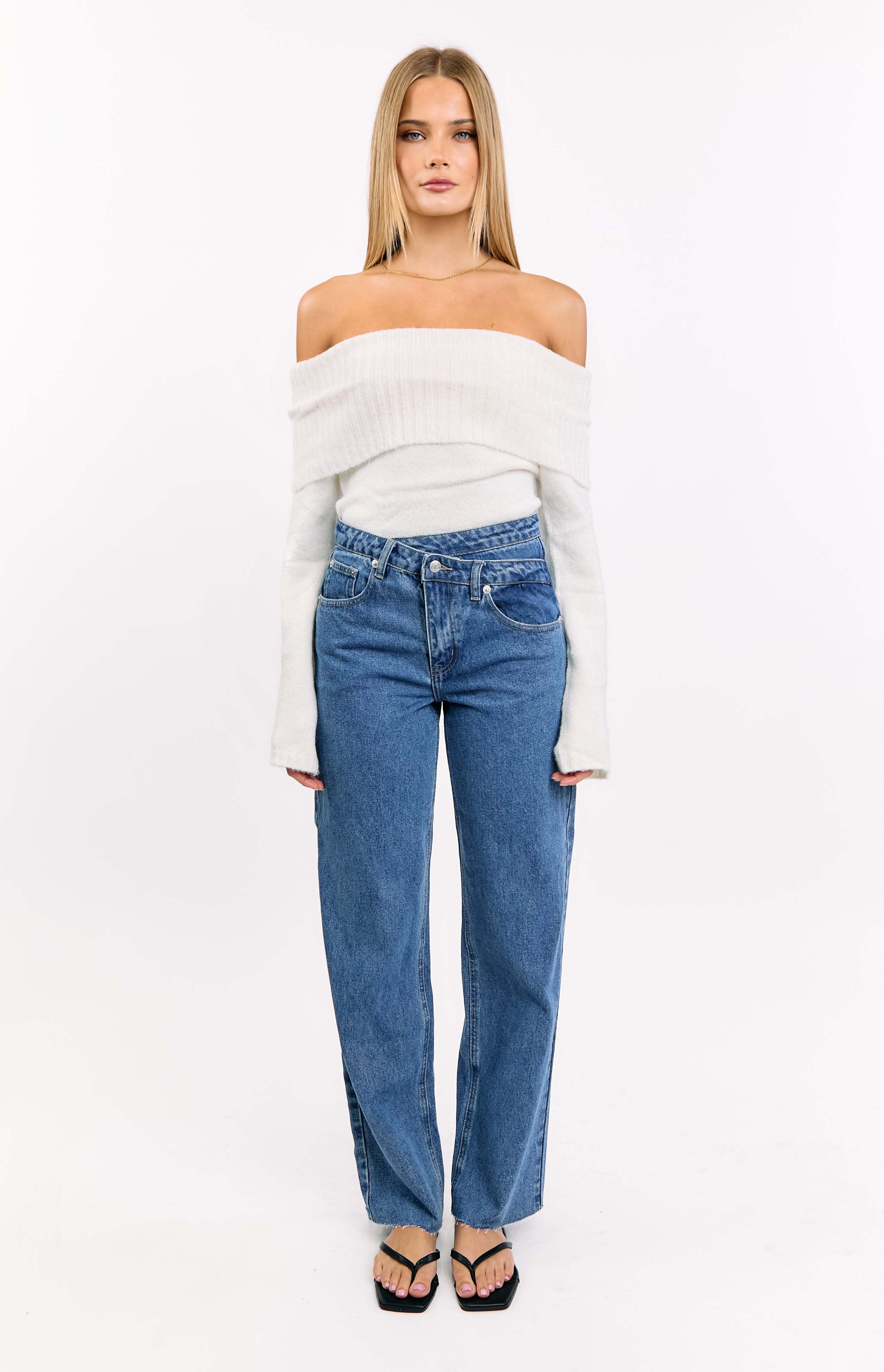 Front view of mid wash blue straight leg jeans with an uneven crossover waistline