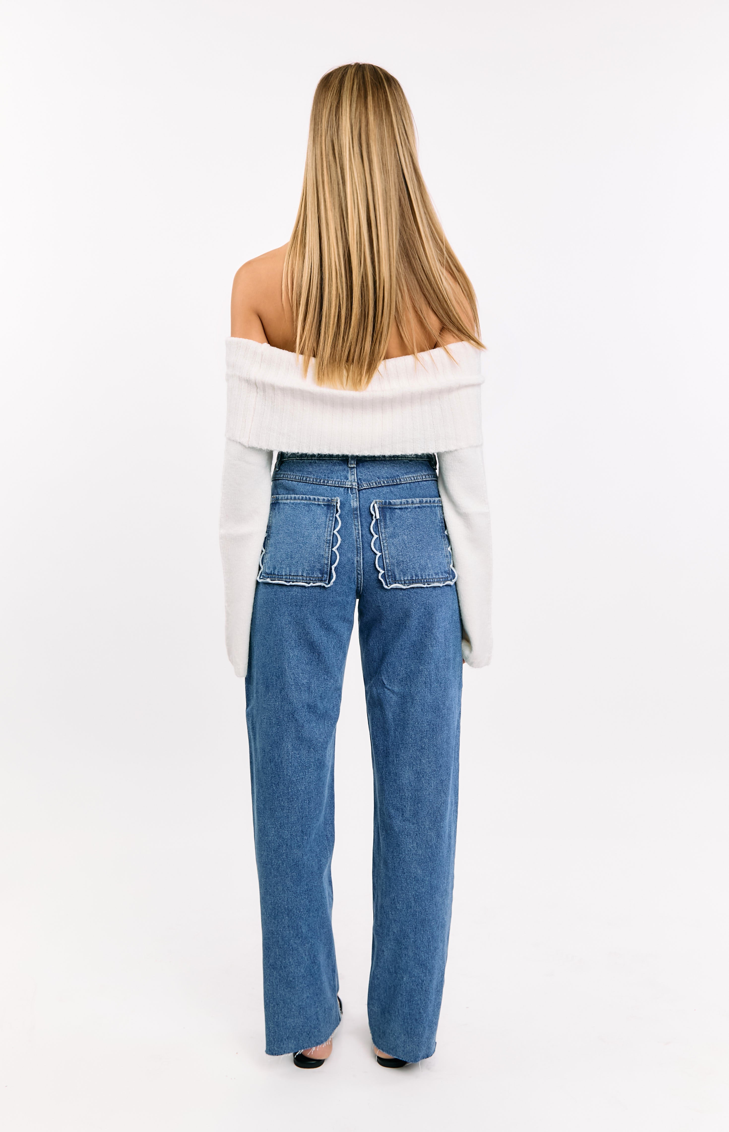 Rear view of mid wash jeans with white trimmed scallop back pockets and raw hem