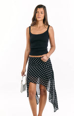 Full view of a black polka dot hanky hem midi skirt with a flowy drape