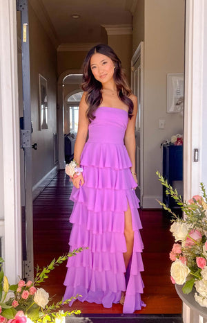 Brunette model wearing a strapless magenta gown with tiered details and a leg slit